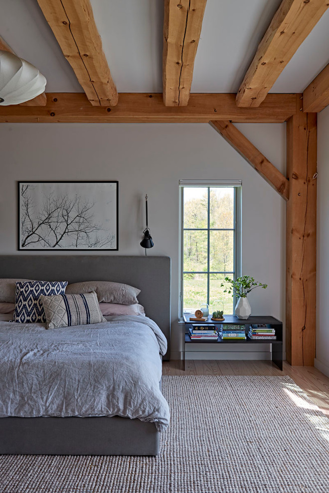 Photo of a large country master bedroom with white walls, light hardwood floors and exposed beam.