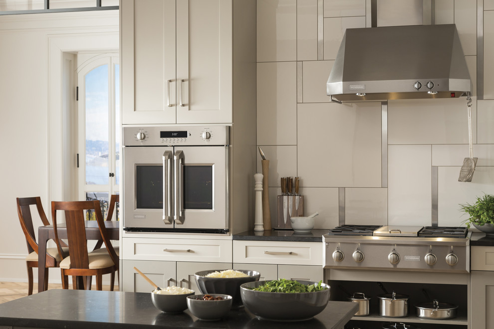 Inspiration for a mid-sized transitional l-shaped medium tone wood floor and brown floor open concept kitchen remodel with stainless steel appliances, an undermount sink, shaker cabinets, white cabinets, granite countertops, white backsplash, porcelain backsplash and an island