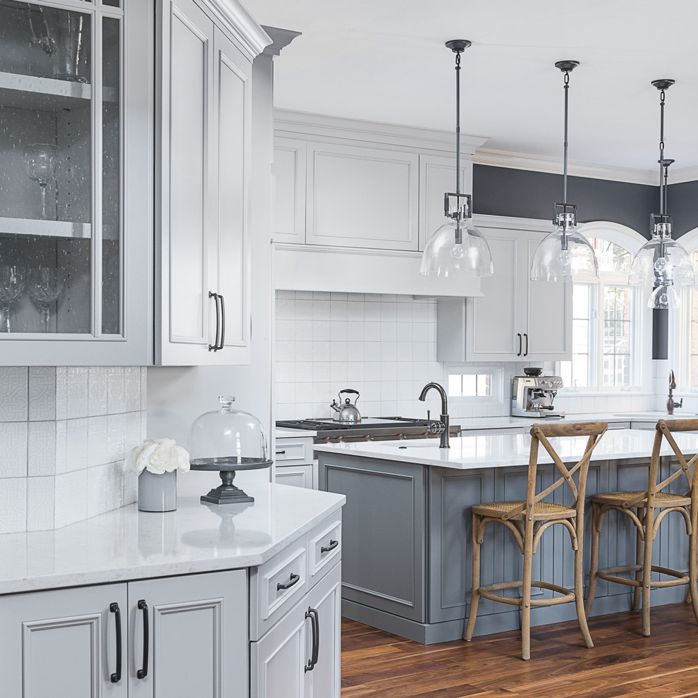 Example of a large transitional l-shaped medium tone wood floor and brown floor eat-in kitchen design in Chicago with an undermount sink, white cabinets, quartz countertops, white backsplash, ceramic backsplash, stainless steel appliances, an island and white countertops