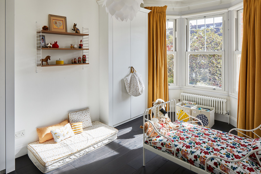 Photo of a small traditional gender-neutral kids' playroom for kids 4-10 years old in London with multi-coloured walls, dark hardwood floors and black floor.