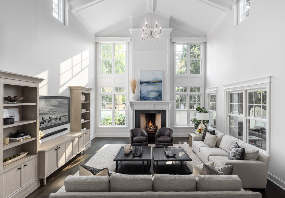 Photo of a large traditional open concept living room in Detroit with grey walls, medium hardwood floors, a standard fireplace, a wood fireplace surround, a wall-mounted tv, brown floor, vaulted and decorative wall panelling.