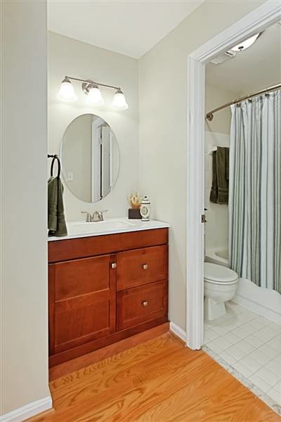 This is an example of a small transitional 3/4 bathroom in DC Metro with an integrated sink, recessed-panel cabinets, medium wood cabinets, marble benchtops, an alcove tub, a one-piece toilet, white tile, ceramic tile, grey walls and medium hardwood floors.