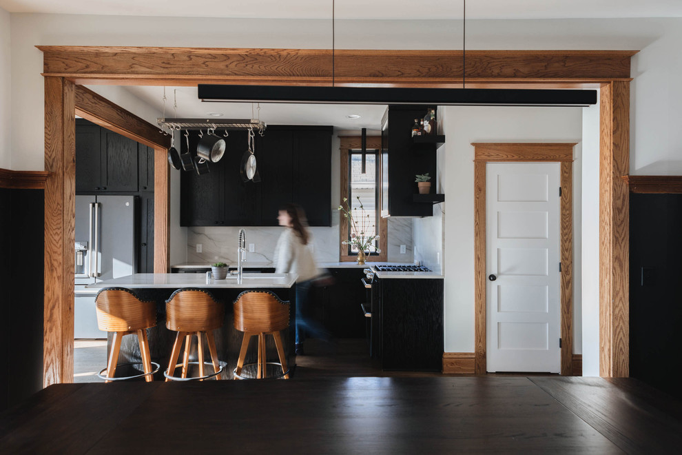 Design ideas for a transitional u-shaped eat-in kitchen in Minneapolis with an undermount sink, recessed-panel cabinets, black cabinets, marble benchtops, white splashback, marble splashback, black appliances, medium hardwood floors, with island, brown floor and white benchtop.