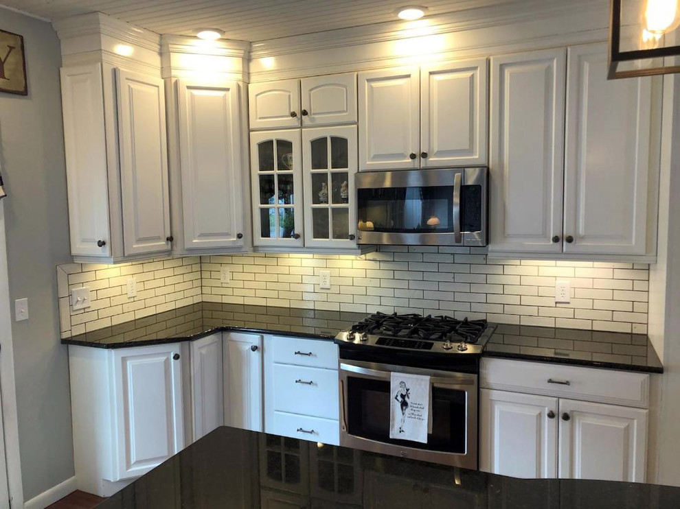 Large transitional l-shaped dark wood floor and brown floor eat-in kitchen photo with raised-panel cabinets, white cabinets, white backsplash, subway tile backsplash, stainless steel appliances, an island, black countertops and quartz countertops