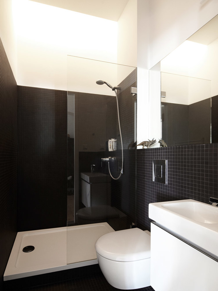 Inspiration for a small contemporary 3/4 bathroom in Berlin with flat-panel cabinets, white cabinets, an alcove shower, a wall-mount toilet, black tile, ceramic tile, white walls and an integrated sink.