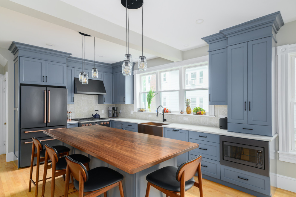 Eat-in kitchen - mid-sized country l-shaped medium tone wood floor and brown floor eat-in kitchen idea in Boston with a farmhouse sink, recessed-panel cabinets, blue cabinets, wood countertops, beige backsplash, ceramic backsplash, black appliances, an island and brown countertops