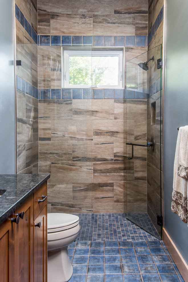 Mid-sized country 3/4 bathroom in Other with recessed-panel cabinets, medium wood cabinets, an alcove shower, brown tile, porcelain tile, grey walls, ceramic floors, an undermount sink, granite benchtops, blue floor, a hinged shower door and black benchtops.