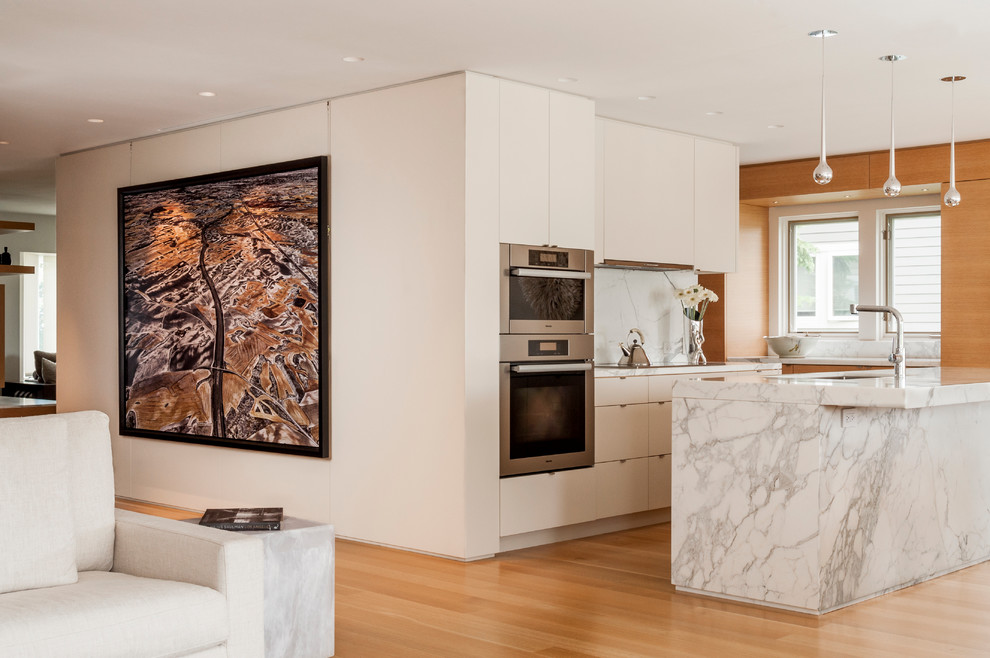 This is an example of a mid-sized scandinavian single-wall eat-in kitchen in Toronto with an undermount sink, flat-panel cabinets, white cabinets, marble benchtops, white splashback, stone slab splashback, panelled appliances, light hardwood floors and with island.