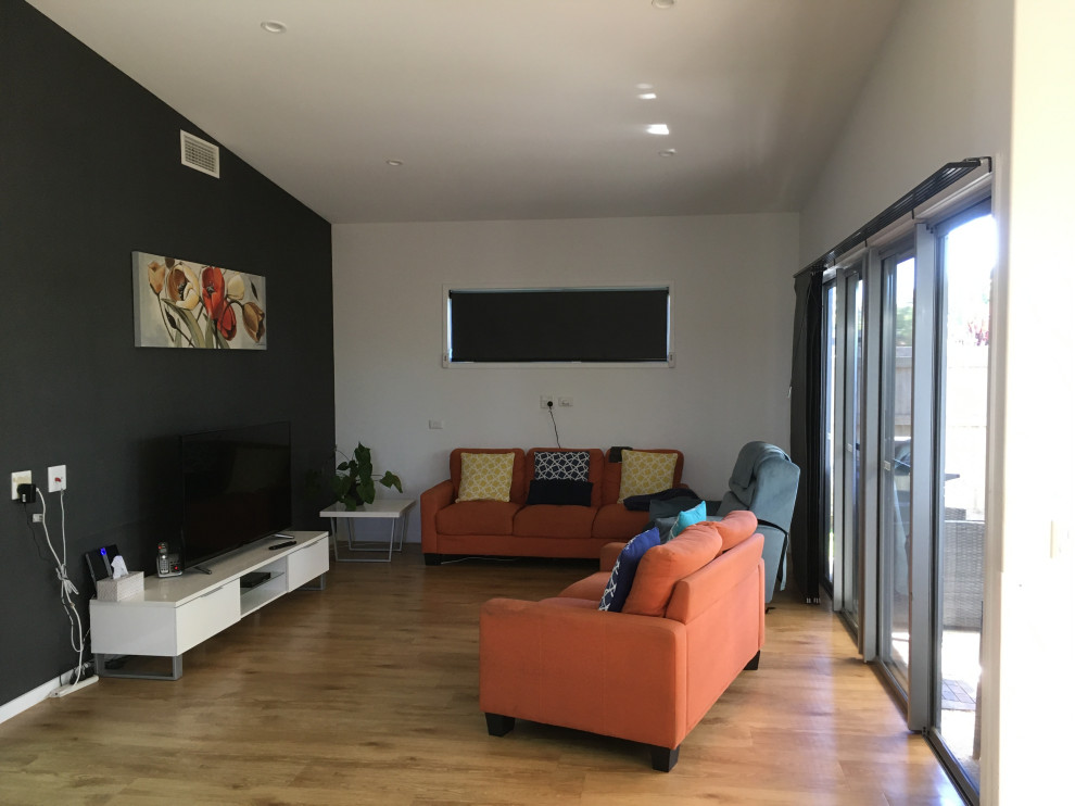 Small contemporary open concept living room in Sunshine Coast with grey walls, plywood floors, a freestanding tv, brown floor, vaulted and panelled walls.
