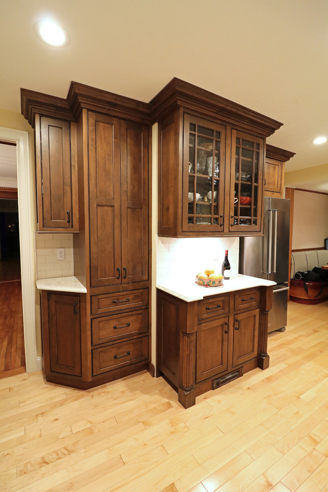 Design ideas for a mid-sized arts and crafts l-shaped kitchen pantry in Boston with a farmhouse sink, beaded inset cabinets, dark wood cabinets, quartz benchtops, beige splashback, travertine splashback, stainless steel appliances, light hardwood floors, no island and beige floor.