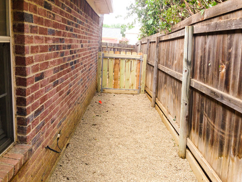 dog run with a wooden privacy fence on one side and a brick house on the other.  Pea gravel is used in the dog run as a ground cover