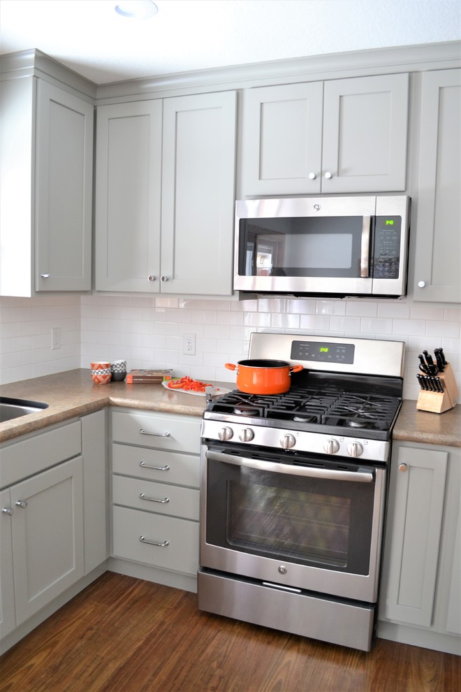 Mid-sized transitional u-shaped vinyl floor and brown floor enclosed kitchen photo with an undermount sink, flat-panel cabinets, gray cabinets, laminate countertops, white backsplash, subway tile backsplash, stainless steel appliances and no island