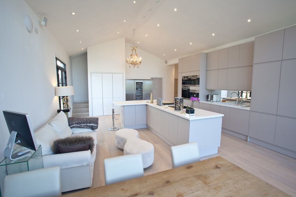 Modern eat-in kitchen in London with a single-bowl sink, flat-panel cabinets, beige cabinets, mirror splashback, stainless steel appliances, light hardwood floors and with island.