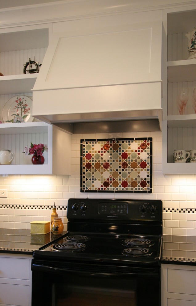 Photo of a small arts and crafts u-shaped eat-in kitchen in Portland with an undermount sink, shaker cabinets, white cabinets, granite benchtops, white splashback, mosaic tile splashback, black appliances, medium hardwood floors and a peninsula.