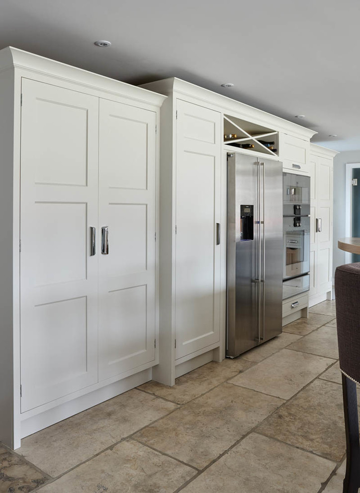 This is an example of a mid-sized traditional galley open plan kitchen in London with recessed-panel cabinets, white cabinets, marble benchtops, white splashback, ceramic splashback, stainless steel appliances, ceramic floors, with island and white benchtop.