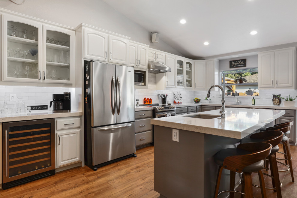 Trendy l-shaped eat-in kitchen photo in Sacramento with a double-bowl sink, white cabinets, quartz countertops, white backsplash, ceramic backsplash, stainless steel appliances, an island and white countertops