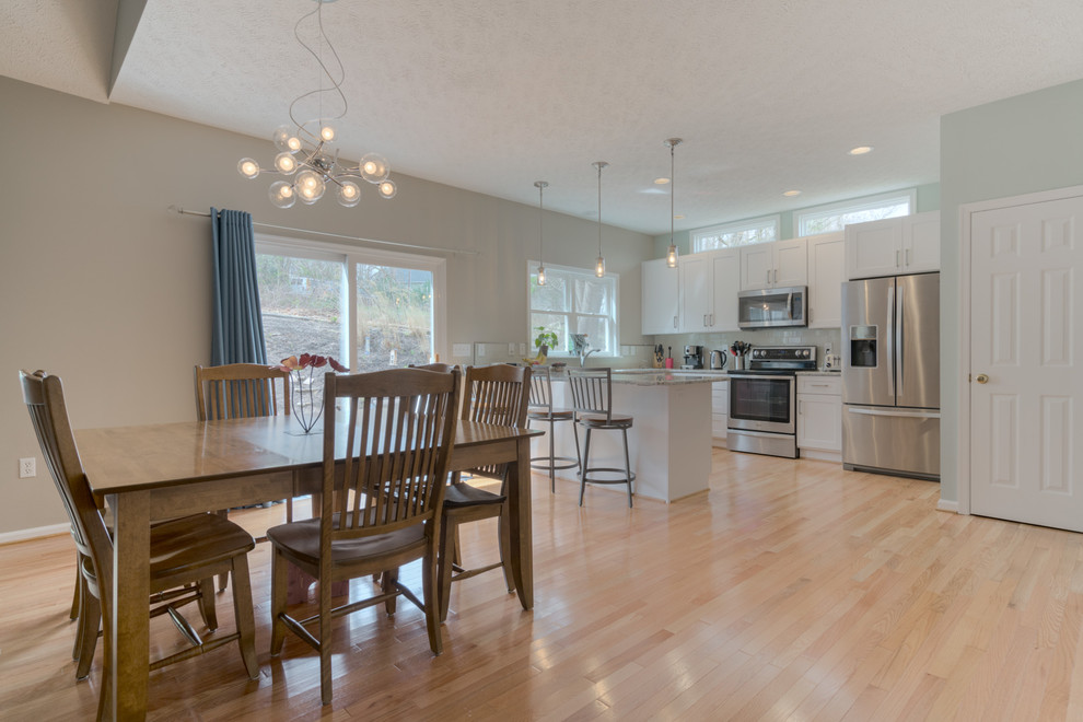 Mid-sized transitional u-shaped light wood floor eat-in kitchen photo with an undermount sink, shaker cabinets, white cabinets, quartz countertops, beige backsplash, glass tile backsplash, stainless steel appliances and a peninsula