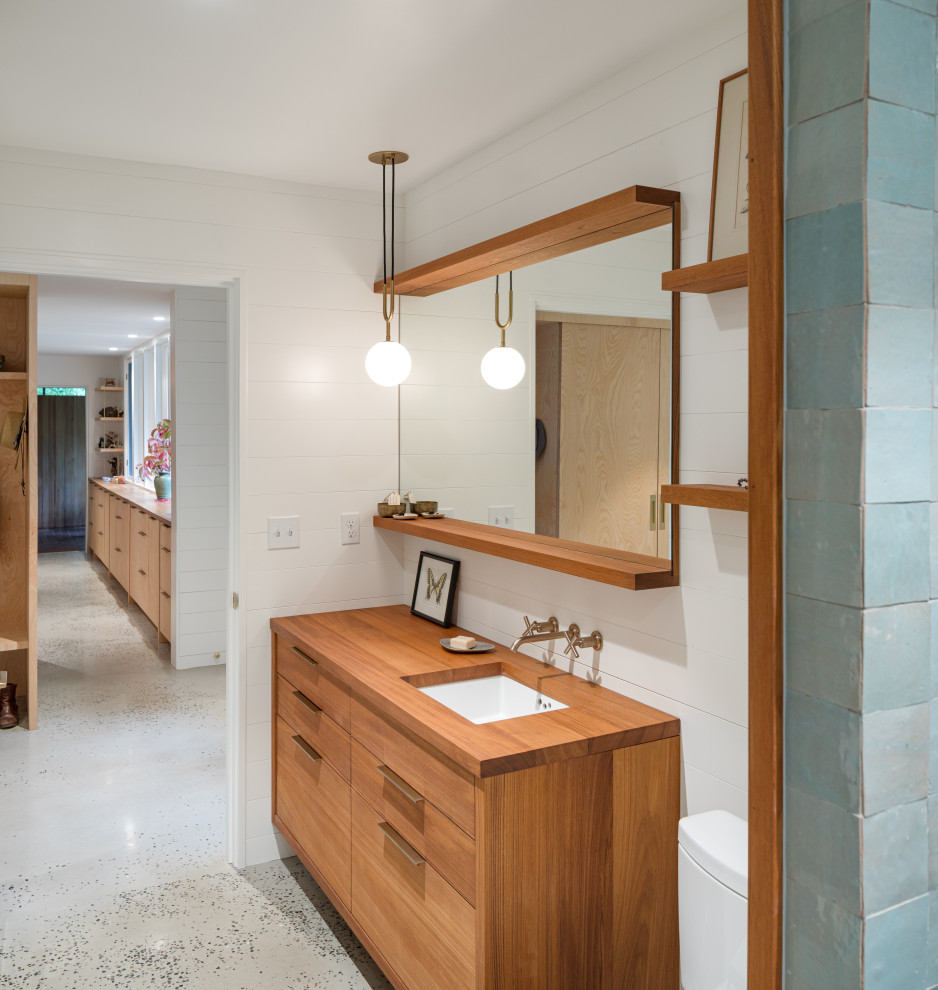 Пример оригинального дизайна: ванная комната в стиле модернизм с плоскими фасадами, открытым душем, унитазом-моноблоком, синей плиткой, керамической плиткой, белыми стенами, бетонным полом, врезной раковиной, столешницей из дерева, серым полом, сиденьем для душа, тумбой под одну раковину, подвесной тумбой и стенами из вагонки