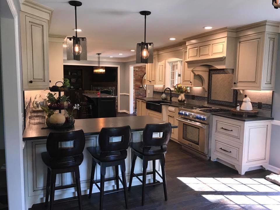 This is an example of a mid-sized country l-shaped eat-in kitchen in Other with a farmhouse sink, distressed cabinets, stainless steel appliances, with island, raised-panel cabinets, soapstone benchtops, grey splashback, ceramic splashback, dark hardwood floors and brown floor.