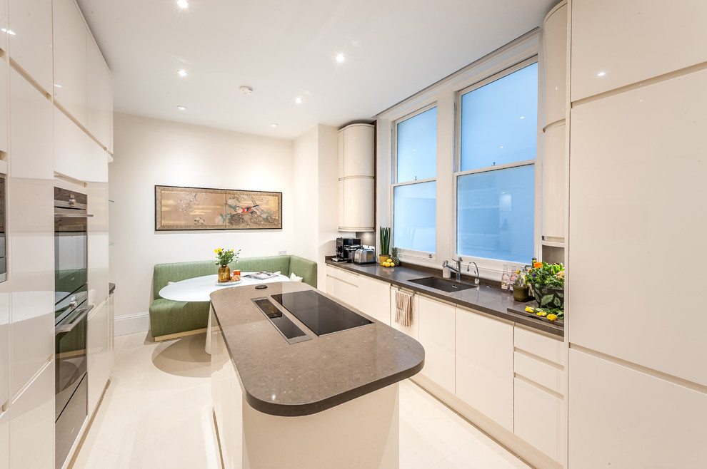 This is an example of a contemporary eat-in kitchen in London with a single-bowl sink, flat-panel cabinets, beige cabinets, with island, beige floor and brown benchtop.