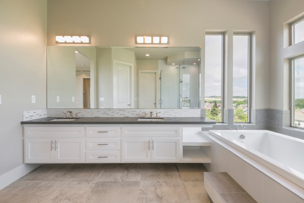 Inspiration for a large contemporary master bathroom in Sacramento with recessed-panel cabinets, white cabinets, a drop-in tub, a corner shower, a two-piece toilet, gray tile, white tile, matchstick tile, beige walls, porcelain floors, an undermount sink, engineered quartz benchtops, beige floor, a hinged shower door and grey benchtops.