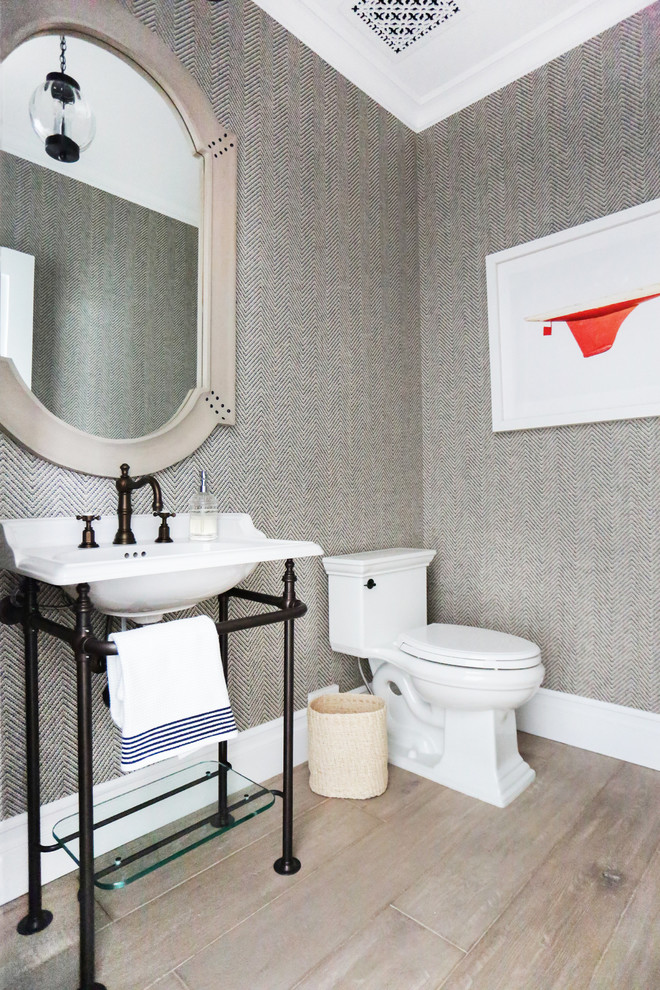 This is an example of a small beach style powder room in Orange County with a console sink, a one-piece toilet and light hardwood floors.