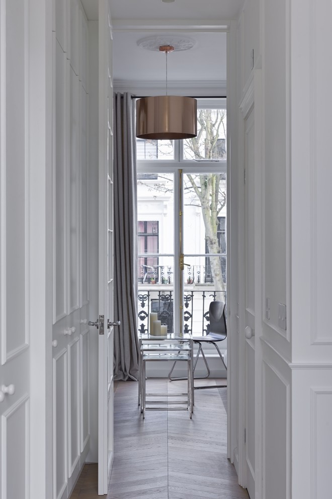 Inspiration for a small traditional gender-neutral walk-in wardrobe in London with flat-panel cabinets, white cabinets, light hardwood floors and brown floor.
