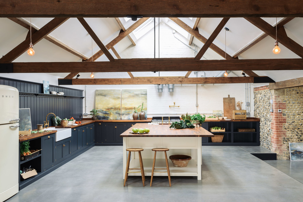 Country kitchen in Other with a farmhouse sink, shaker cabinets, blue cabinets, wood benchtops, blue splashback, timber splashback, concrete floors, with island, grey floor and brown benchtop.
