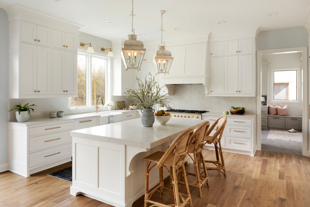 Inspiration for an expansive traditional u-shaped eat-in kitchen in Minneapolis with a farmhouse sink, recessed-panel cabinets, white cabinets, quartz benchtops, white splashback, engineered quartz splashback, white appliances, light hardwood floors, with island, brown floor and white benchtop.