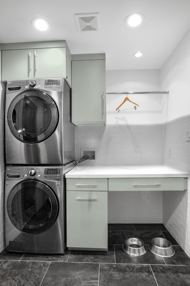Mid-sized midcentury single-wall dedicated laundry room in Houston with flat-panel cabinets, grey cabinets, solid surface benchtops, white walls, porcelain floors, a stacked washer and dryer and grey floor.