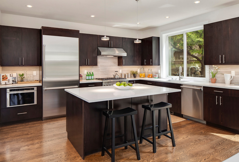 Photo of a contemporary l-shaped kitchen in Seattle with an undermount sink, flat-panel cabinets, dark wood cabinets, beige splashback, stainless steel appliances, medium hardwood floors, with island and limestone splashback.