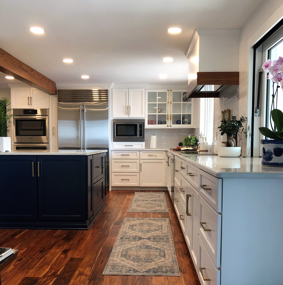 Inspiration for a mid-sized transitional l-shaped medium tone wood floor and brown floor kitchen pantry remodel with an undermount sink, flat-panel cabinets, blue cabinets, quartz countertops, white backsplash, subway tile backsplash, stainless steel appliances, an island and gray countertops