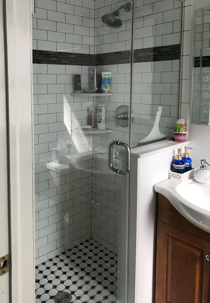 Photo of a small eclectic 3/4 bathroom in New York with raised-panel cabinets, medium wood cabinets, a two-piece toilet, white tile, subway tile, white walls, ceramic floors, a console sink, white floor, a hinged shower door, an alcove shower, solid surface benchtops and white benchtops.