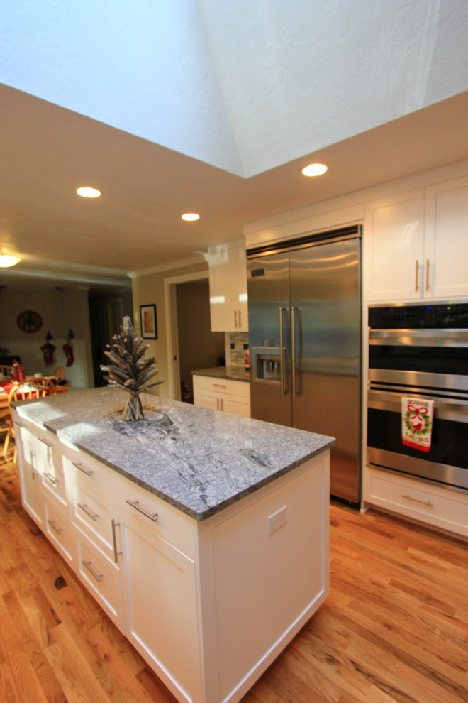 Large transitional u-shaped light wood floor open concept kitchen photo with an undermount sink, shaker cabinets, white cabinets, granite countertops, multicolored backsplash, mosaic tile backsplash, stainless steel appliances and an island