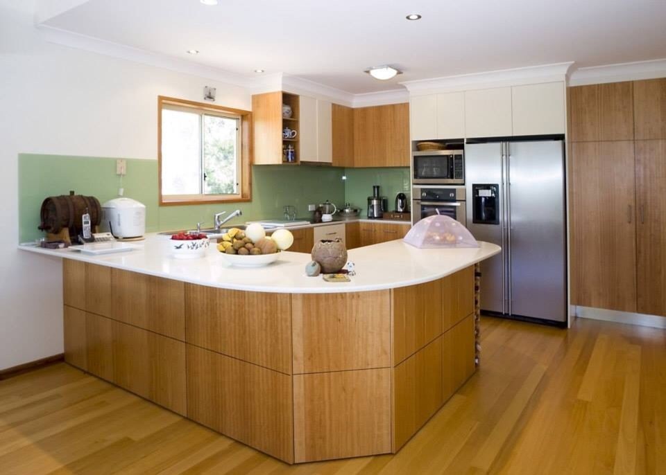 Photo of a large contemporary u-shaped kitchen pantry in Brisbane with a double-bowl sink, flat-panel cabinets, light wood cabinets, solid surface benchtops, green splashback, glass sheet splashback, stainless steel appliances and medium hardwood floors.