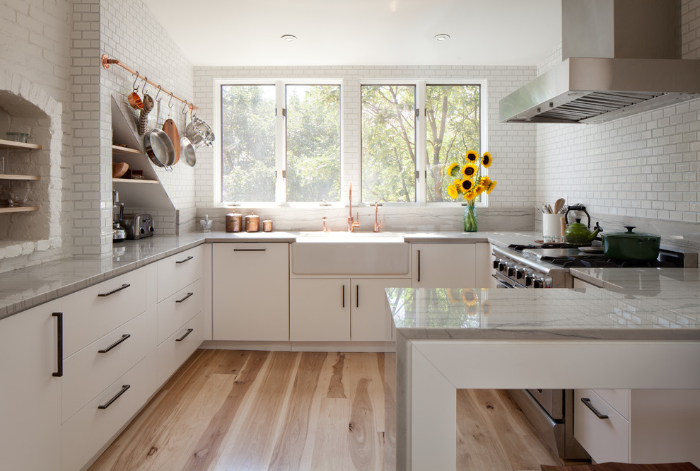 Photo of a contemporary u-shaped separate kitchen in Boston with medium hardwood floors, a farmhouse sink, flat-panel cabinets, white cabinets, marble benchtops, white splashback, subway tile splashback, stainless steel appliances and no island.