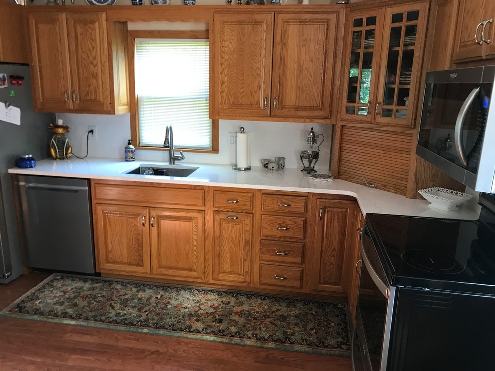 Photo of a small traditional l-shaped separate kitchen in Cedar Rapids with an undermount sink, raised-panel cabinets, medium wood cabinets, quartz benchtops, white splashback, subway tile splashback, stainless steel appliances, carpet, no island, multi-coloured floor and white benchtop.