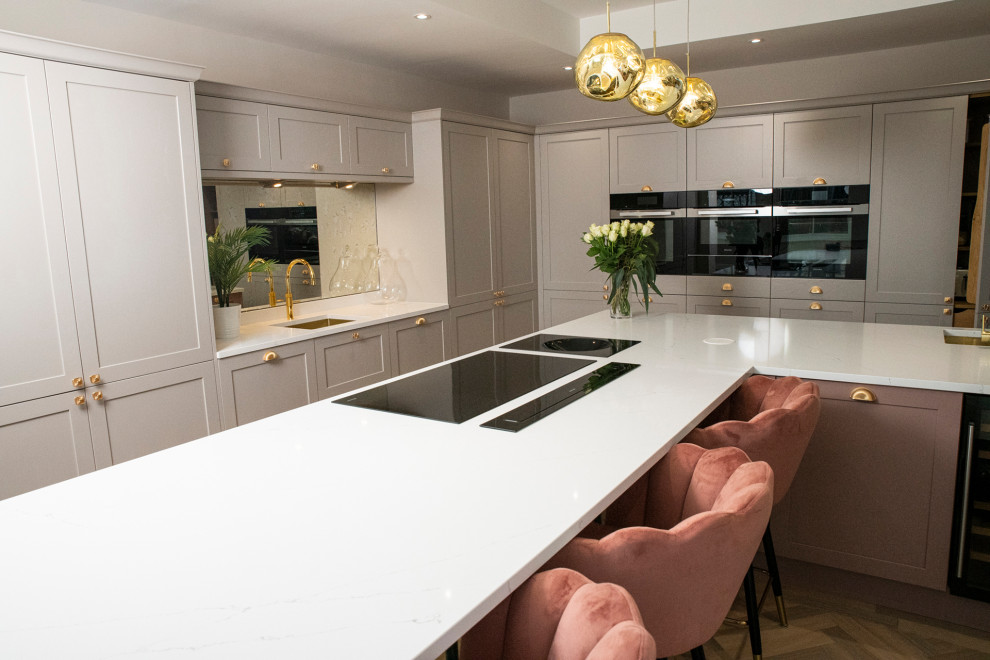 This is an example of a large traditional l-shaped open plan kitchen in Manchester with an undermount sink, shaker cabinets, pink cabinets, quartzite benchtops, metallic splashback, mirror splashback, panelled appliances, ceramic floors, with island, grey floor and white benchtop.