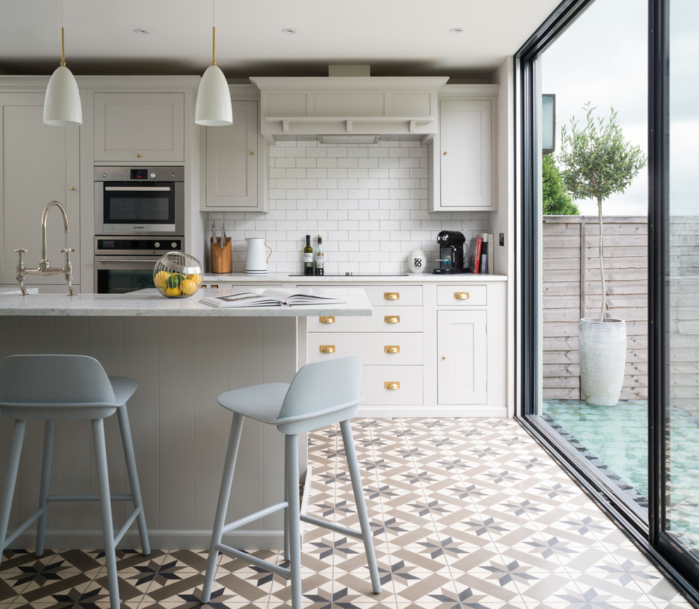 Transitional kitchen in London with shaker cabinets, grey cabinets, white splashback, subway tile splashback, with island, stainless steel appliances and multi-coloured floor.