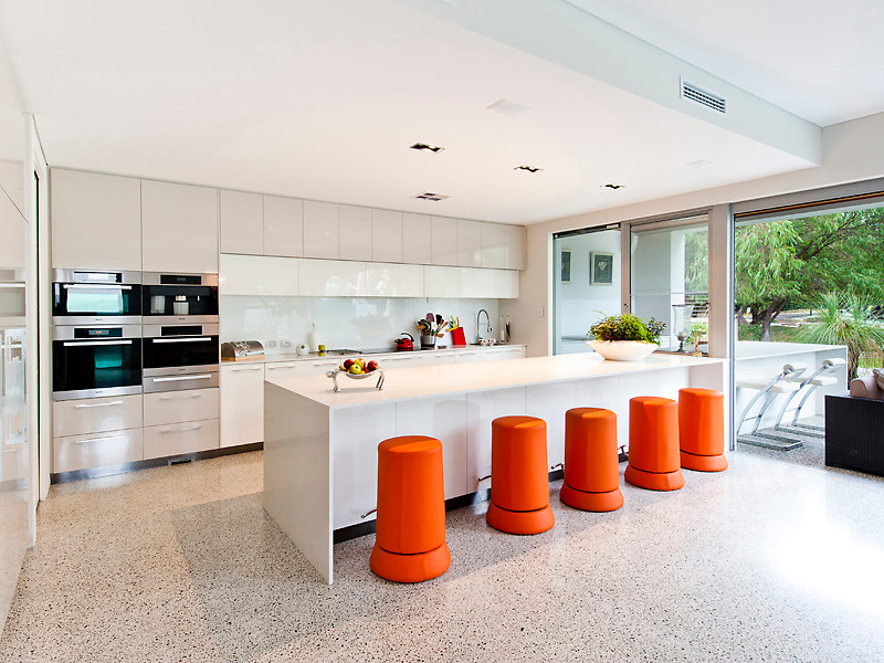 Design ideas for a large modern galley open plan kitchen in Perth with a single-bowl sink, flat-panel cabinets, white cabinets, quartz benchtops, white splashback, glass sheet splashback, stainless steel appliances, concrete floors, with island and grey floor.