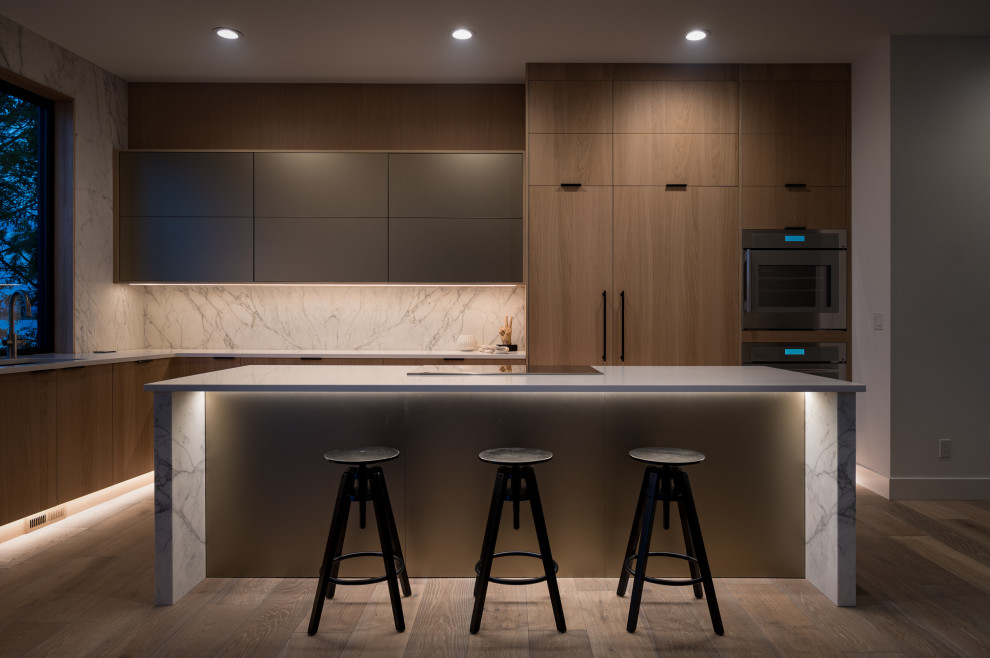 Photo of a large contemporary l-shaped open plan kitchen in Phoenix with a submerged sink, flat-panel cabinets, light wood cabinets, engineered stone countertops, white splashback, stone slab splashback, integrated appliances, light hardwood flooring, an island, brown floors and white worktops.