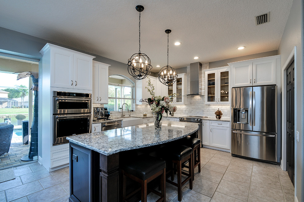 Example of a transitional ceramic tile kitchen design in Tampa with a farmhouse sink, white cabinets, white backsplash, stone tile backsplash, stainless steel appliances and an island