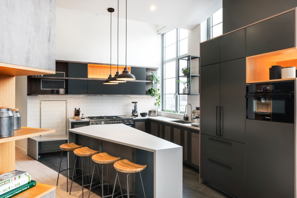 Design ideas for a large industrial u-shaped eat-in kitchen in New York with an undermount sink, flat-panel cabinets, grey cabinets, quartz benchtops, white splashback, subway tile splashback, black appliances, with island and white benchtop.