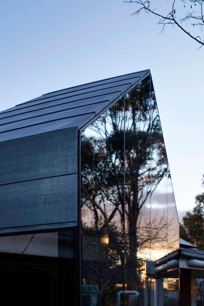 Photo of a small contemporary two-storey glass brown house exterior in Hobart with a gable roof and a metal roof.