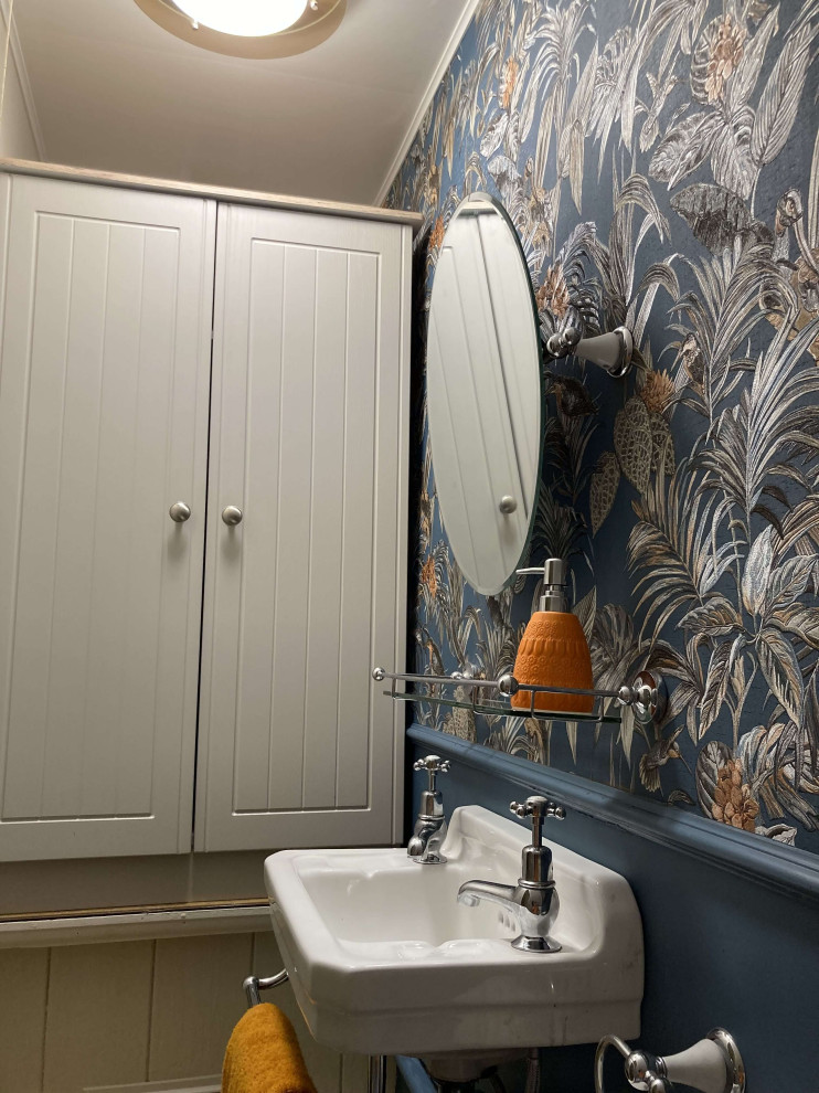 Источник вдохновения для домашнего уюта: маленький туалет в викторианском стиле с унитазом-моноблоком, синими стенами, полом из ламината, подвесной раковиной, коричневым полом, акцентной стеной и обоями на стенах для на участке и в саду