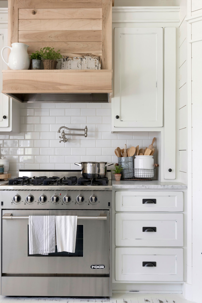 This is an example of a mid-sized country u-shaped eat-in kitchen in Minneapolis with a farmhouse sink, beaded inset cabinets, white cabinets, white splashback, timber splashback, painted wood floors, with island, white floor and white benchtop.