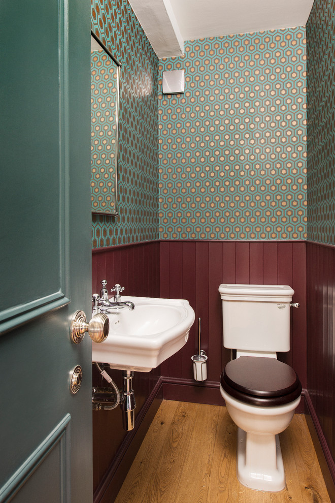 Small traditional powder room in London with a two-piece toilet, light hardwood floors, a wall-mount sink, brown floor and multi-coloured walls.
