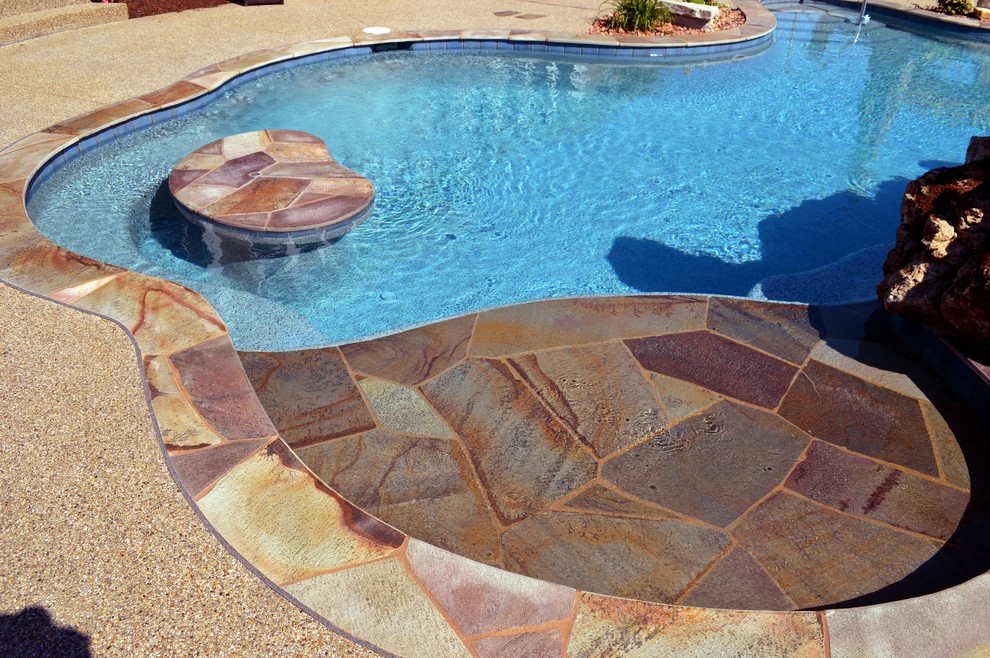 Free form pool with stone table, sun shelf, water feature, and outdoor kitchen,