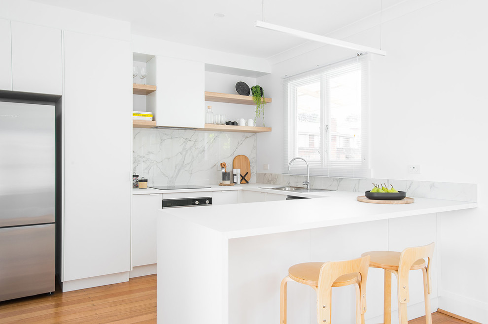 This is an example of a scandinavian u-shaped kitchen in Hobart with a drop-in sink, flat-panel cabinets, white cabinets, grey splashback, stone slab splashback, stainless steel appliances, medium hardwood floors, brown floor and white benchtop.