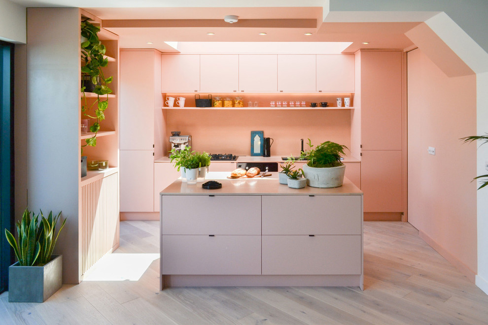 This is an example of a mid-sized modern single-wall kitchen in London with an undermount sink, flat-panel cabinets, pink splashback, black appliances, with island, grey floor and light hardwood floors.
